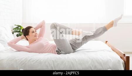 Morgen Fitness. Sportliche Dame, fit Übungen, auf dem Bett zu Hause liegen, Panorama Stockfoto