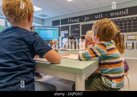 NIJMEGEN/Niederlande - September 13, 2019: Kinder im Klassenzimmer sitzen, hören auf die teacherBlack boaed und Smart Board sichtbar Stockfoto