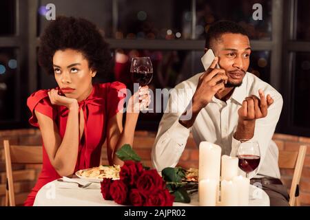 Schlechtes Datum. Gelangweilt African American Girl Warten, während Freund am Telefon sprechen mit Abendessen im Restaurant. Stockfoto