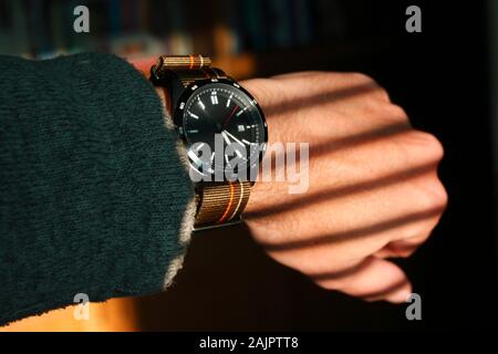 Nahaufnahme des Handgelenks des Mannes mit Uhr und parallelen Schatten von Jalousien über die Hand. Konzeptfoto, das Zeit, warten, im/Geduld, Gefangenschaft vorschlägt. Stockfoto