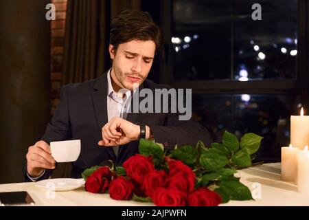 Mann mit Blumen wartende Freundin im Restaurant nervös, trinken Kaffee, Kontrolle der Zeit Stockfoto