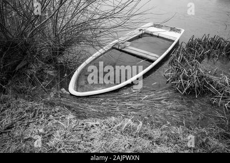 Ein versunkenes Ruderboot liegt am Ufer eines kleinen Sees Stockfoto