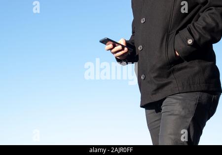 Mann mit einem blauen Smartphone. Seitenansicht Schuss mit einer Hand in der Jackentasche. Leeren Bereich des Himmels Stockfoto