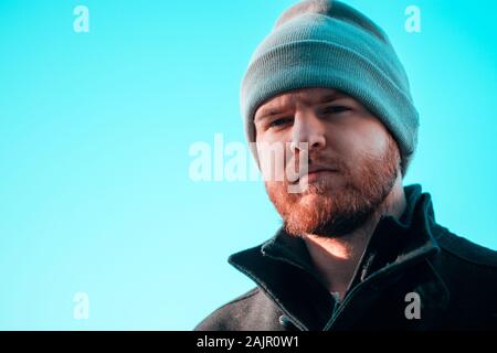 Bärtiger Mann mit einer Mütze in die Kamera schaut mit einem ernsten Blick, Licht blauer Himmel. Ernsthafte Betrachtung denken Stimmung Stockfoto