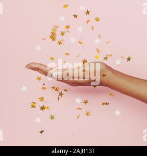 Gold Konfetti Sterne Dekoration in weiblicher Hand auf Pastell rosa Hintergrund Stockfoto