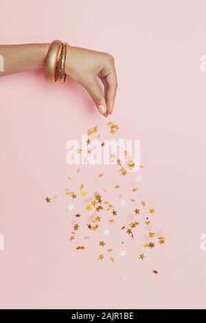 Schöne weibliche Hand streams funkelnden Gold Sterne Konfetti auf rosa Hintergrund Stockfoto