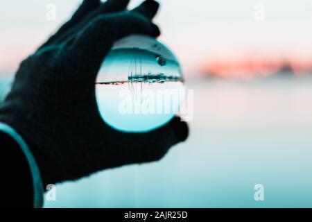 Hand mit einem Handschuh Holding eine Glaskugel, marina Segelboote auf dem Kopf in der Kugel. Kalte Winter Foto Stockfoto