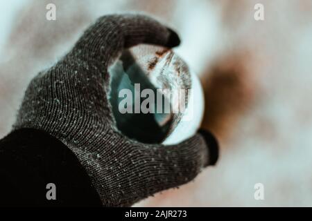 Hand mit einem Kristall Glas Kugel. Konzentrieren Sie sich auf die Hand. Verschwommen Formen in der Kugel. kalten Winter Handschuh Foto Stockfoto