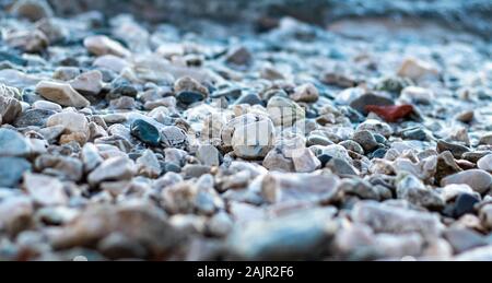 Kies Kiesel am Strand Ufer, kalten Foto. Nasse Steine Sonnenlicht reflektieren, viele verschiedene Farben von runden Kieseln Stockfoto