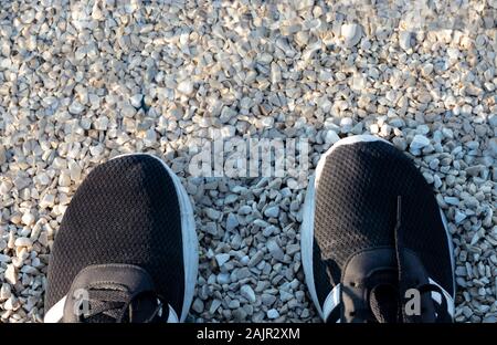 Zwei schwarze Schuhe in der Nähe des Meeres, auf felsigen Kiesstrand. Kristallklare Meer Wasser kaum spürbar Stockfoto