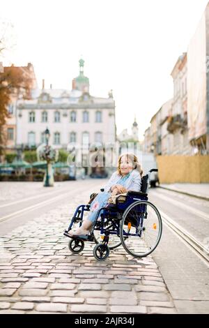 Schöne behinderte Frau im Rollstuhl lächelnd in die Kamera bei einem Spaziergang in der Altstadt. Stockfoto