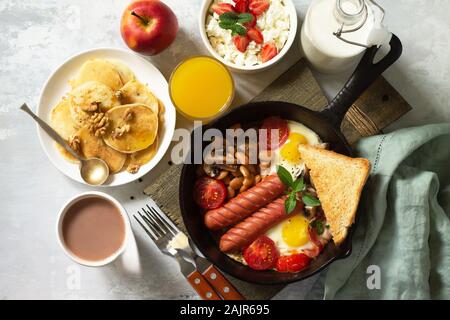 Keto Frühstück: Spiegeleier, Würstchen, Bohnen, Speck, Pilzen, gegrillte Toast, Orangensaft, Quark, Pfannkuchen und Kakao auf einem Tisch aus Stein Stockfoto