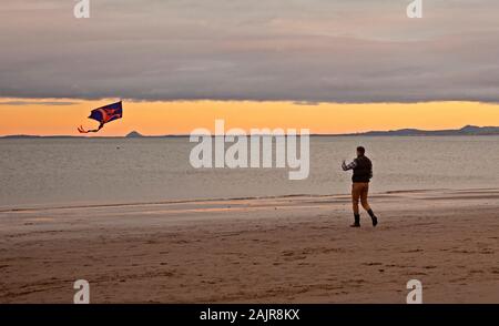 Portobello, Edinburgh, Schottland, Großbritannien. Januar 2020. Eine steife Brise kurz vor Sonnenuntergang in Portobello nach dem Wind früher von 30 km/h gab diesem Mann die Möglichkeit, seinen Drachen an der Küste des Sandstrandes zu fliegen. Stockfoto