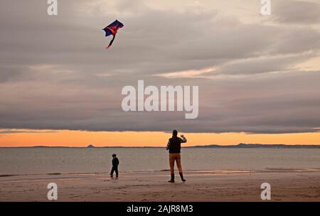 Portobello, Edinburgh, Schottland, Großbritannien. Januar 2020. Eine steife Brise kurz vor Sonnenuntergang in Portobello nach dem Wind früher von 30 km/h gab diesem Mann die Möglichkeit, seinen Drachen an der Küste des Sandstrandes zu fliegen. Stockfoto