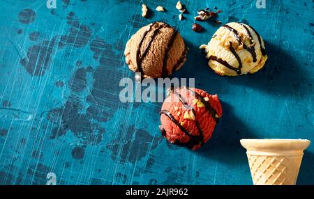 Drei verschiedene aromatisiert Eisportionierer beträufelt mit Schokolade und gehackten Nüssen auf einem blauen Mosaikfliesen Hintergrund mit Kopie Raum und Wafer Kegel Stockfoto