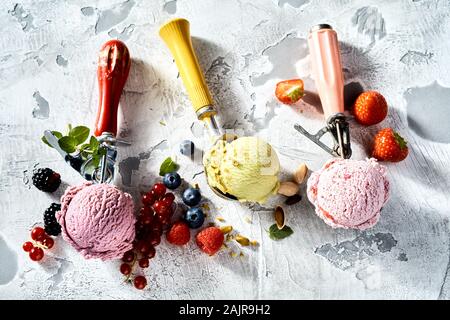 Verschiedene Eissorten in Metall Schaufeln durch Frische rote Johannisbeere, Himbeere, Erdbeere, Brombeere, Heidelbeere und Pistazie Zutaten umgeben Stockfoto