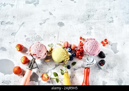 Drei verschiedene Geschmacksrichtungen von Eis in Metall Schaufeln mit Pistazien, gemischte Beeren und Erdbeere von oben gesehen auf einen gerissenen weißen Lack ba Stockfoto