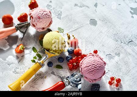 Drei Eis Schaufeln mit verschiedenen Aromen von mixed Berry und Pistazie Eis in ihnen werden mit frischem Obst und kopieren Raum umgeben Stockfoto