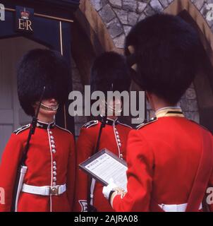 In den 1960er Jahren trug die historische, uniformierte Wache der Königin ihre Bärenmützen und roten Tuniken, die an ihren Sentry-Posten standen und von ihrem Offizier auf dem Ceremonial Most Noble Order of the Garter, der in Windsor Castle, Windsor, England, Großbritannien abgehalten wurde, angesprochen wurden. Der Edelmann der Strumpfband ist ein von Art Edward III. 1348 gegründeter Ritterorden. Stockfoto