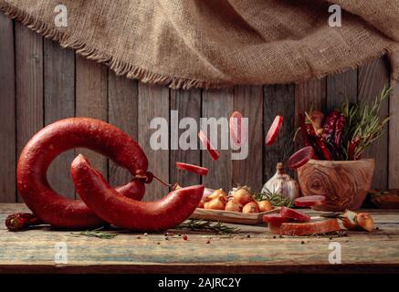 Sandwich hausgemacht geräucherter Salami. Auf einem alten Holztisch Wurst mit Brot, Rosmarin, Zwiebel, Knoblauch und Pfeffer. Stockfoto