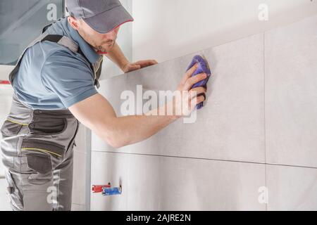 Home Improvement Thema. Kaukasische Auftragnehmer Arbeiter in seinem 30s Keramische Fliesen im Badezimmer. Stockfoto