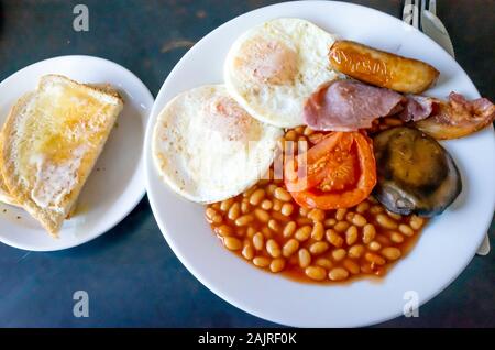 Englisches Frühstück Speck zwei Spiegeleier gebackene Bohnen gegrillte Tomate Pilz mit weißen Toast Wurst Stockfoto