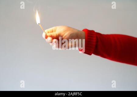 Frau gekleidet in Rot mit einem Match auf einem grauen Hintergrund beleuchtet. Konzept der Brand- und entspricht. Stockfoto