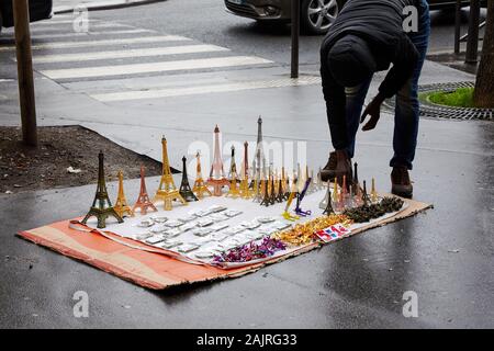 Mann verkauf Miniatur Eiffel Towers, ausgebreitet auf einem Stück Karton auf einer nassen Straße; Paris, Frankreich Stockfoto