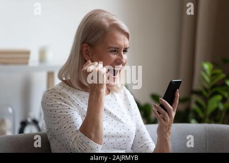 Aufgeregt reife Frau fühlen mit guten Nachrichten auf Handys überglücklich Stockfoto