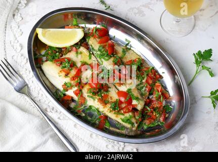 Gegrillter Meeresbarsch auf einem Teller mit frischen Tomaten und mit Petersilie und Zitrone dekoriert. Draufsicht Stockfoto