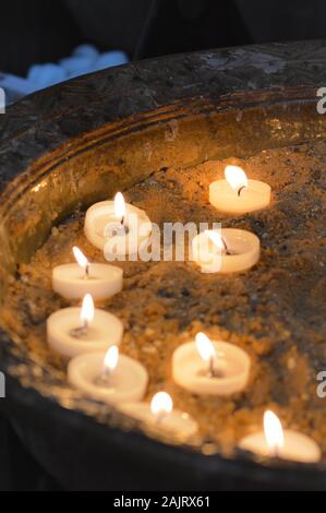 Weiße Teelichtkerzen mit Flamme in der Kirchengedenkstätte Stockfoto