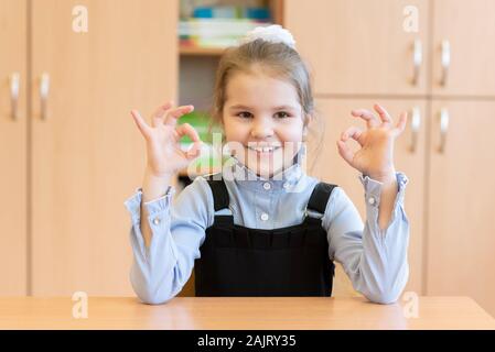 Mädchen Schülerin sitzt an ihrem Schreibtisch und zeigt die Zeichen in Ordnung. Stockfoto