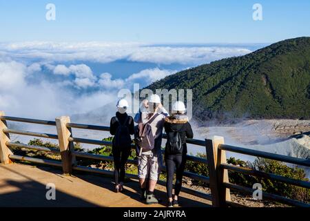 Touristen mit Schutzhelmen beobachten Rauch, steigen aus dem Vulkan Poas. Stockfoto