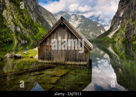 Eine Holzhütte, verwendet als Bootshaus, das Wasser der Obersee durch hohe Alpen in Schönau am Königssee in Bayern, Deutschland umgeben. Stockfoto