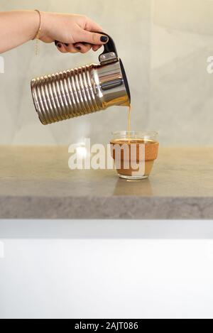 Die Frau ist strömenden heißen Kaffee aus der Kaffeemaschine in wiederverwendbare Glas Kaffeetasse auf dem marmortisch in den Morgen. Stockfoto