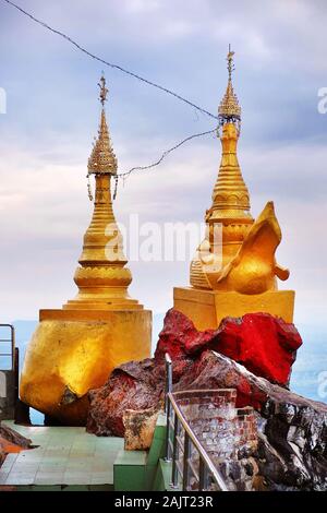 Goldene und rote Türme auf den Wänden der buddhistischen Tempel des Mount Popa, in Myanmar, vor blauem Himmel. Stockfoto