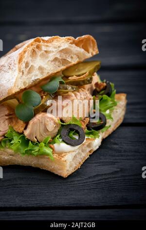 American fast food. Saftiger Thunfisch Sandwich mit Käse, Salat und Oliven auf einem dunklen Hintergrund. Club Essen Stockfoto