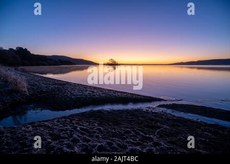 Winter Sonnenaufgang an einem ruhigen See mit Insel, Bach und frostigen Ufer. Burleigh Sands, Loch Leven National Nature Reserve, Schottland, Großbritannien. Stockfoto