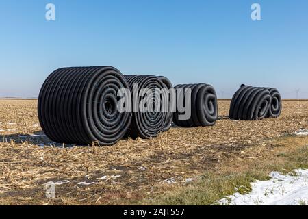 Aufgerollte Rollen aus schwarzem perforiertem Kunststoff Ablassrohr, Feld Fliesen, sitzen in Feld nach der Ernte bereit, u-begraben werden im Winter Stockfoto