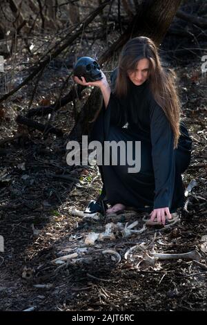 Frau in schwarzen Roben mit Haufen von grossen wilden tierischen Knochen in der Mitte des Waldes. Magie und Hexerei Konzept. Stockfoto