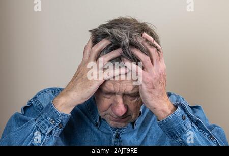 Kopf und Schultern Portrait eines älteren kaukasischen Mann mit Kopf in den Händen und Suchen gedrückt Stockfoto