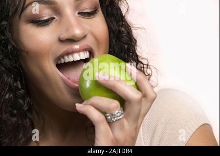 Nahaufnahme, Porträt einer Latino Frau in einen grünen Apfel beißen auf weißem Hintergrund Stockfoto