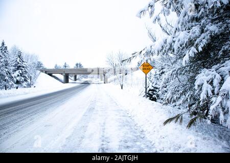 Rutschige verschneite Straße und Wald im Central Wisconsin im Dezember mit Stop vor Zeichen Stockfoto