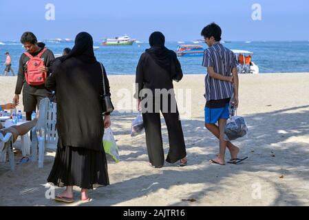 Muslimische Frau, die traditionelle schwarze Kleidung mit Harem Gaucho pants und Hijab headwear am Pattaya Beach Thailand Stockfoto