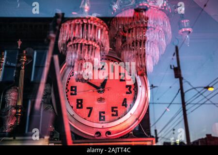 Eine alte antike Uhr und Glaslüster beleuchtet in rosa Licht in einem Schaufenster Stockfoto