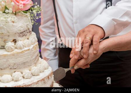 Älteres Paar gekleidet Luxuriös zusammen schneiden eine schöne 3 Tier Hochzeitstag Kuchen. Konzept der Union und ewige Liebe. Selektive konzentrieren. Stockfoto