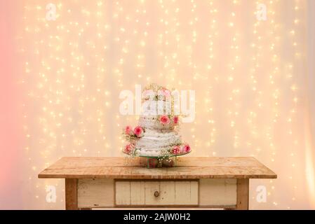 In der Nähe von wunderschönen weißen Baum Stufe Kuchen mit frischen Blumen mit ziemlich licht und Laternen leuchten im Hintergrund auf einem hölzernen rustikalen Tisch. Selec Stockfoto