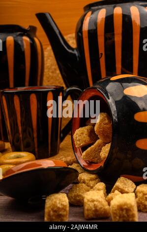 Stücke von Brown Sugar, Sugar Bowl, und Töpferei vor dem Hintergrund von grobem Homespun Tuch. Nahaufnahme Stockfoto