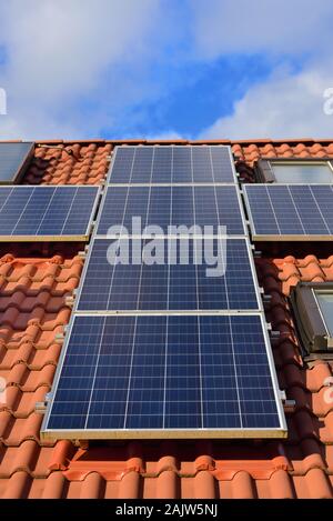 Hintergrund und close-up eine Solaranlage auf dem Dach eines Einfamilienhauses mit roten Dachziegeln, gegen einen blauen Himmel mit Wolken und Sonnenschein für Energie aus s Stockfoto