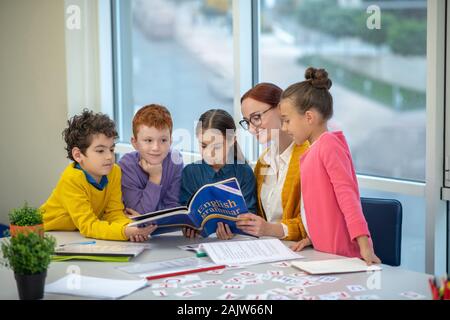 Kinder ein Buch lesen während ihres Englisch Klasse Stockfoto